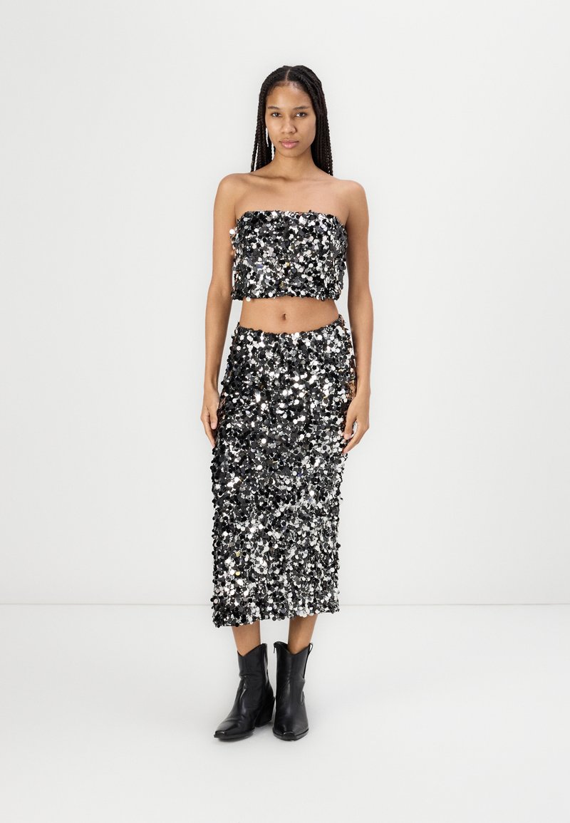 Conjunto de dos piezas en negro y plateado con lentejuelas que incluye un top sin tirantes y una falda de longitud media, combinado con botas negras hasta el tobillo. Textura suave.