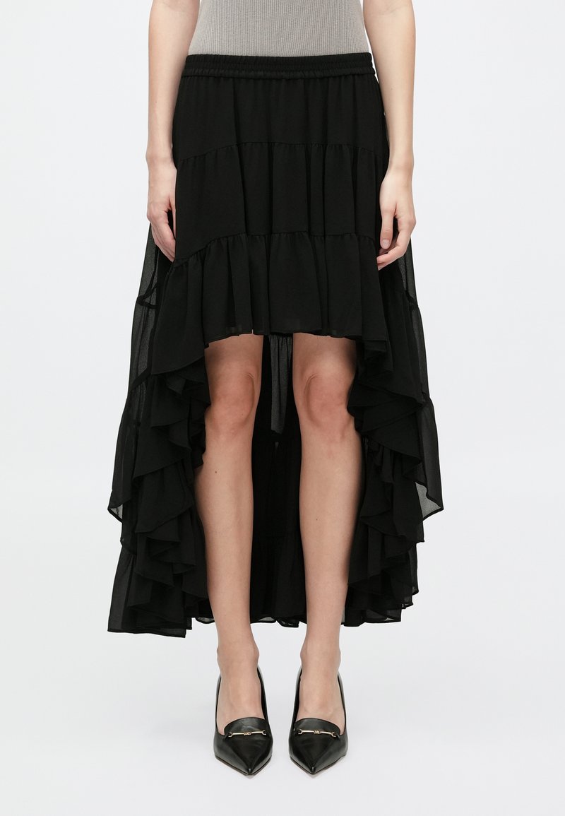 Jupe noire à ourlet asymétrique en chiffon superposé, dotée d'un design à volants. Associée à des escarpins noirs à talons pointus pour un contraste.