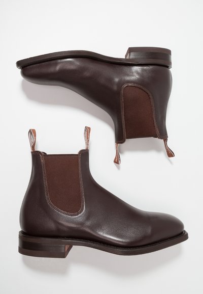 Brown leather Chelsea boots with elastic side panels, rounded toe, and pull tabs. Smooth texture and contrasting brown accents. Flat heel.