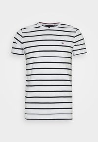 Biała koszulka z krótkim rękawem w poziome, równomiernie rozmieszczone czarne paski oraz małe logo w kolorach czerwonym, białym i niebieskim na piersi.