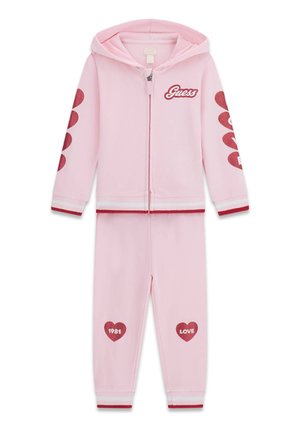 Różowy dwu-częściowy dres dziecięcy z bluzą na suwak z kapturem, czerwonymi wzorami serc na rękawach i spodniach, logo "Guess" na piersi.
