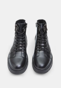 Botas de cuero negro hasta el tobillo con punta redondeada, cordones en la parte delantera, cremalleras laterales y suelas texturizadas para mayor agarre y soporte.
