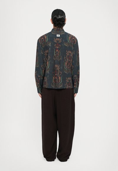 Long-sleeve shirt in dark blue with a floral pattern in brown and green, paired with loose-fitting dark pants. Textured fabric, buttoned collar.