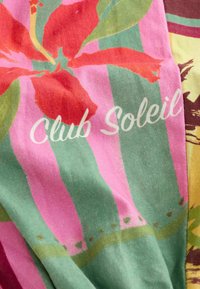 Tissu avec rayures verticales vertes et roses, grande fleur d'hibiscus rouge et texte blanc « Club Soleil ».
