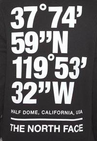Černá mikina s velkým bílým textem zobrazujícím souřadnice, název místa "Half Dome, Kalifornie, USA" a název značky "THE NORTH FACE."