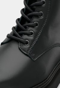 Κοντινό πλάνο μαύρης δερμάτινης μπότες με στρογγυλά μαύρα κορδόνια περασμένα μέσα από μεταλλικά οπτικά και λεπτομερή ραφή.