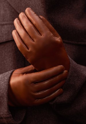 Brown leather gloves with a smooth texture, featuring four elongated fingers and a simple design. They are held together against a dark background.