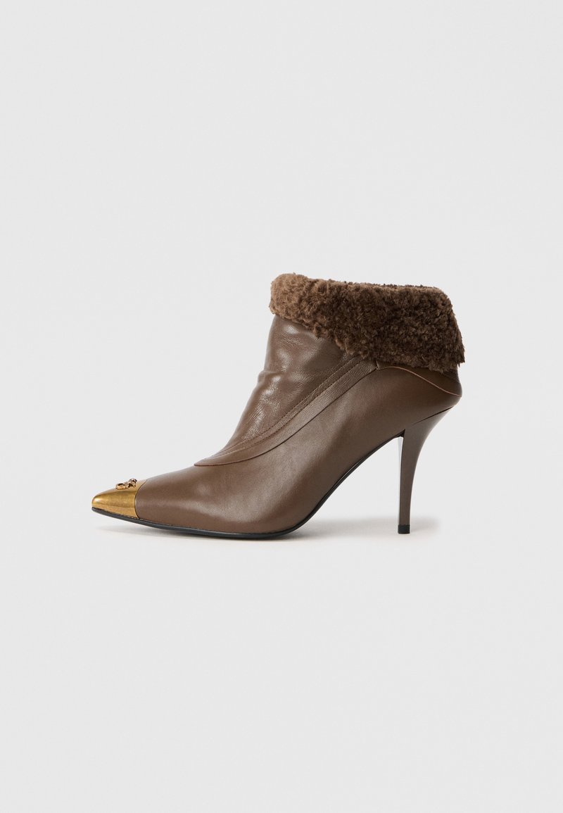 Browns ādas potītes zābaks ar pūkainu brūnu malējo daļu, smailu purngalu ar metālisku zelta galu un stiletto papēdi.