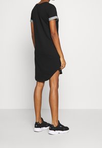Czarna sukienka t-shirt z podwiniętymi szarymi rękawami, bocznymi rozcięciami i luźnym krojem. Noszona z czarnymi trampkami z białymi podeszwami.