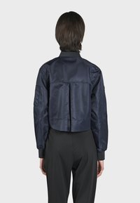 Navyfärgad cropped satin bomberjacka med ribbad krage och ärmslut. Har en veckad ryggdetalj och en sidficka på ärmen. Slät textur.