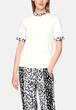 Woman wearing a white short-sleeve shirt with black and white animal print trim and matching black and white animal print pants.