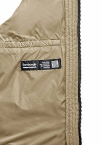 Beige pufferjacketintern met een zwart label met een QR-code en tekst, een gladde textuur en stiksels langs de randen.
