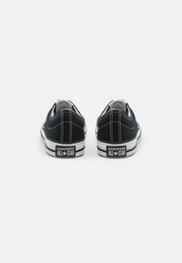 Sorte lerret lave sneakers med hvite sting og gummisåler, med Converse All Star-logo på hælen og klassiske stripete detaljer.
