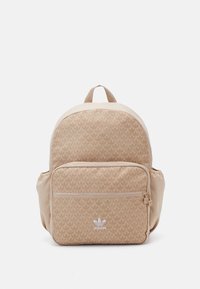 Béžový látkový batoh s celoplošným listovým vzorem, přední kapsou na zip a horním poutkem pro nošení. Bílé logo na přední straně.