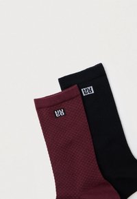 Dva páry ponožiek: jeden bordový s textúrovaným vzorom a jeden úplne čierny. Obe majú malé štvorcové logá v bielej farbe.