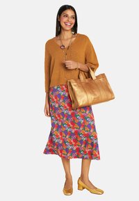 Brauner Strickpullover, Blumen-Midirock in lebhaften Farben, gelbe Blockabsatzschuhe und eine große metallic-goldene Tragetasche.