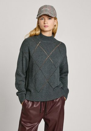 Maglione grigio lavorato a maglia con tagli a rombo, collo alto e polsini a coste, abbinato a pantaloni in pelle ecologica bordeaux e un berretto a quadri.