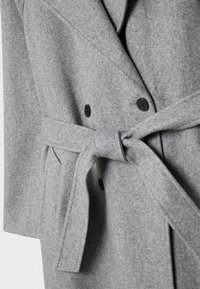 Manteau en laine grise avec des boutons noirs, une ceinture en tissu nouée et des poches latérales, montrant un gros plan de la section médiane.