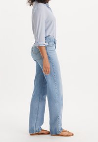 Světle modré džíny s vysokým pasem a rovnými nohavicemi. Nosené s pruhovanou košili na knoflíky. Materiál vypadá jako denim a obsahuje klasické zadní kapsy.