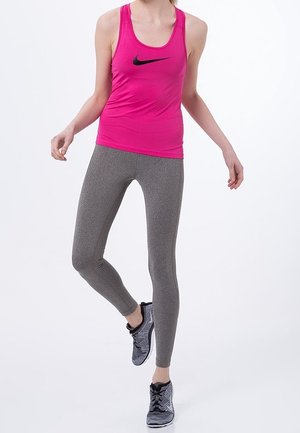 Roze mouwloos Nike tanktop met zwart logo, gecombineerd met grijze leggings. Model draagt zwart-grijze sportschoenen. Eenvoudig, aangesloten ontwerp.