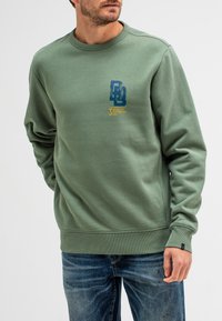 Olijfgroene sweatshirt met geribbelde manchetten en zoom. Heeft een blauw en geel grafisch dessin op de voorkant, gemaakt van zachte katoen.