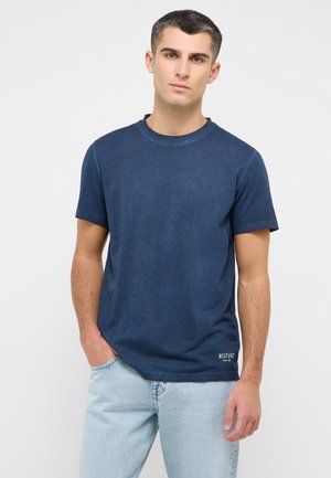 T-shirt en coton bleu marine à manches courtes, col rond, avec un branding discret sur l'ourlet inférieur. Texture lisse et coupe décontractée.