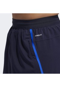 Shorts de sport navy avec une rayure bleue, dotés d'une taille élastique et de l'étiquette "PRIMEBLUE" sur le côté. Texture lisse.