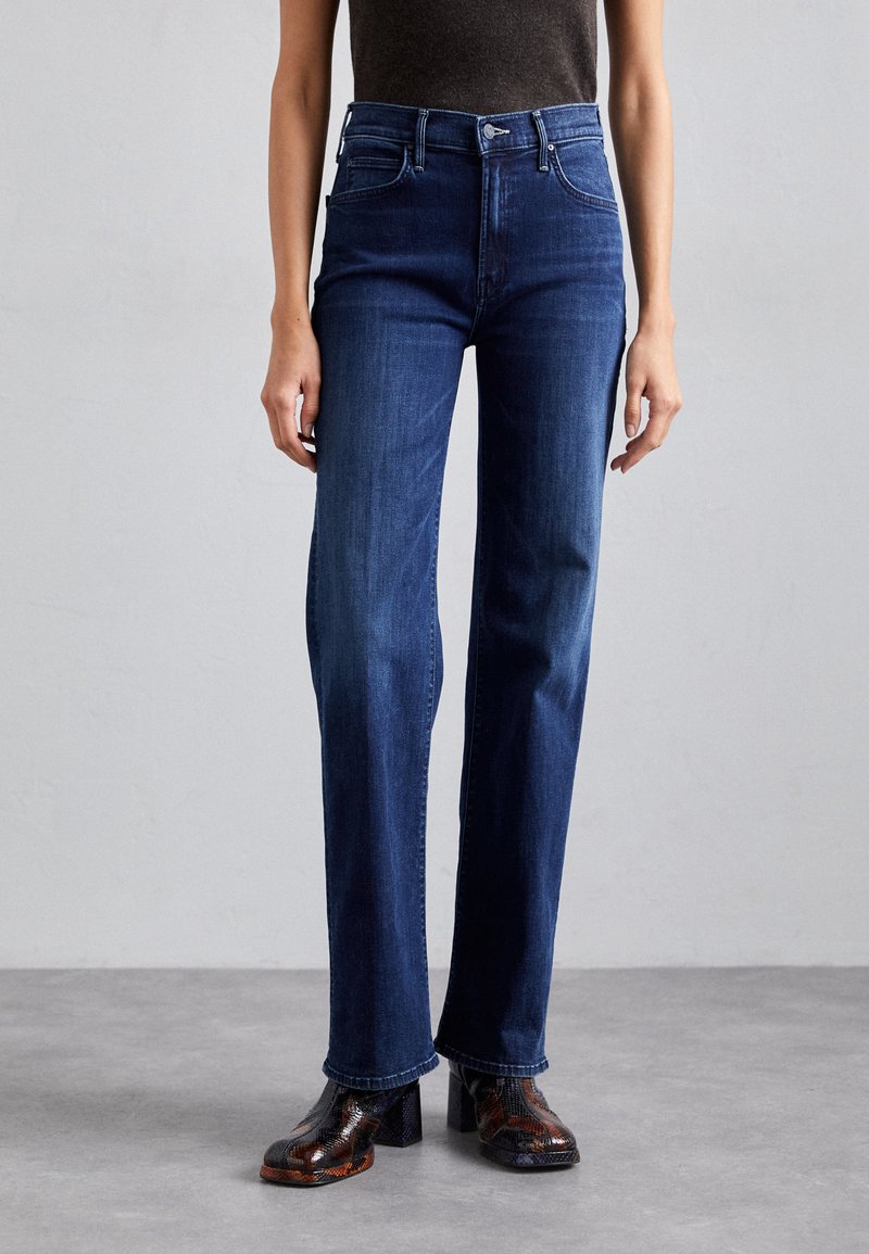 Jeans ajustados azul oscuro con cintura alta, diseño de pierna recta, cinco bolsillos y costuras en contraste. Combinados con zapatos de tacón alto texturizados.