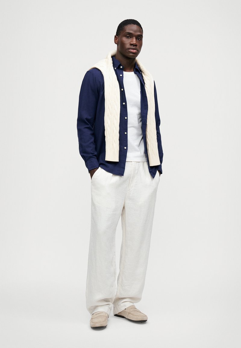 Navy button-up skjorte, hvid t-shirt, cremet kabelstrikket tørklæde, løse hvide linnedbukser, beige loafers. Struktureret stof og afslappet pasform.