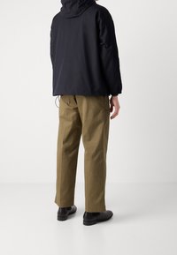 Námořnická bunda, volný střih, s kapucí a elastickými manžetami; doplněná olivově zelenými kalhotami; outfit dokončují černé boty.