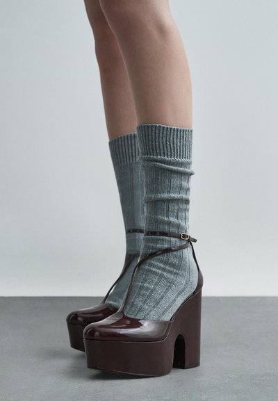 Buty na platformie w błyszczącym burgundowym wykończeniu, w połączeniu z prążkowanymi szarymi skarpetkami. W butach zastosowano design z paskiem T i małym zapięciem.