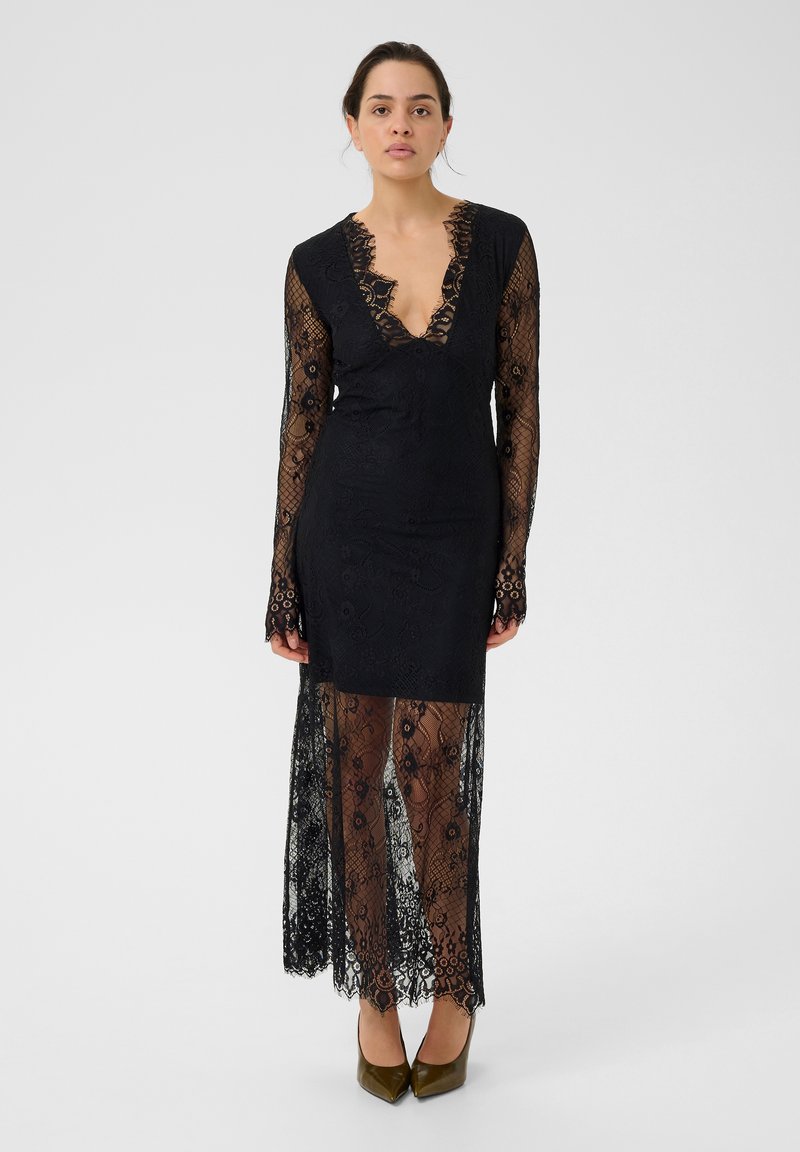Robe en dentelle noire avec de longues manches transparentes et un décolleté en V profond. Présente des motifs floraux complexes et une silhouette ajustée, avec une superposition en dentelle plus longue.