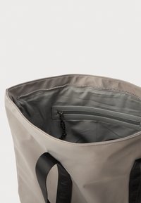 Bež torba s crnim ručkama, otvorenog vrha s unutarnjim zip zatvaračem i crnom špagom, glatka tkanina unutrašnjosti.