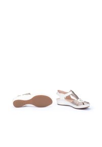 Sandales compensées blanches avec un design à t-strap, des accents métalliques et une semelle texturée. Matériel doux avec des coutures décoratives et un détail floral.