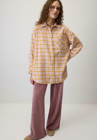 Sárga és levendula kockás, gombos ing elülső zsebbel, laza rózsaszín bársonynadrággal párosítva. Puha tapintás és laza szabás.