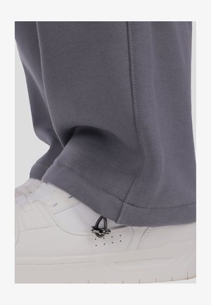 Hallid dressipüksid katavad valget tossu, millel on musta riistvaralist osa ja detailid pahkluu lähedal. Kangas paistab pehme ja sile.