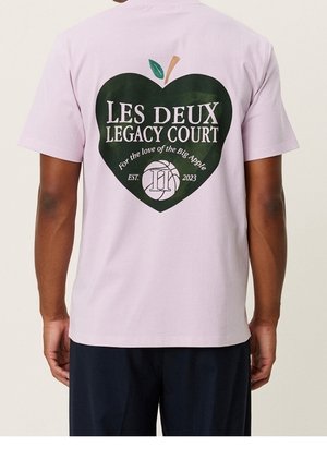 Liliowa bawełniana koszulka z dużym zielonym sercem oraz napisem "LES DEUX LEGACY COURT" i wzorem jabłka, widok z tyłu.