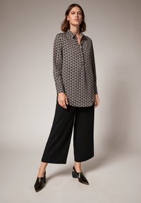 Knoop-up shirt met een geometrisch zwart-wit patroon, gecombineerd met zwarte wijde broek en donkere hakken.