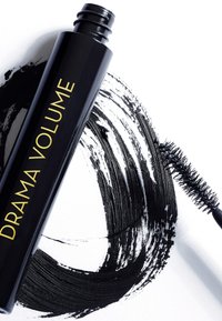 Tubetto di mascara nero con testo dorato "DRAMA VOLUME," accompagnato da un pennello nero e una pennellata stilizzata nera su sfondo bianco.