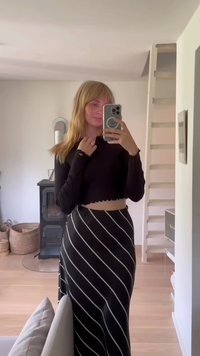 Top preto cropped de manga longa com bainha recortada, combinado com uma saia preta de cintura alta com riscas diagonais brancas.