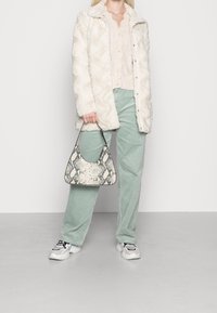 Chaqueta de piel sintética color crema, suéter ligero de punto, pantalones de pana verde menta y un bolso de serpiente con forma curvada, combinados con zapatillas blancas.