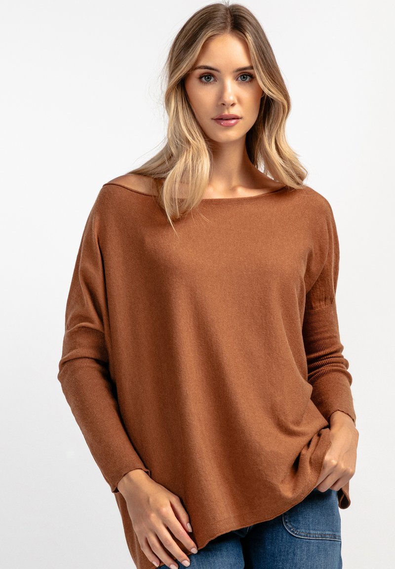 Luźny brązowy sweter z miękkiej przędzy, z szerokim dekoltem i ściągaczami na rękawach, w zestawie z dżinsami.