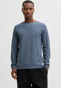 Langermet blå strikket genser med teksturert finish, rund hals og sydd detaljer på skuldrene, kombinert med svarte bukser.