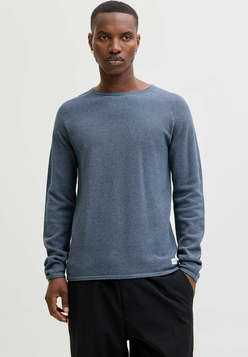 Langermet blå strikket genser med teksturert finish, rund hals og sydd detaljer på skuldrene, kombinert med svarte bukser.