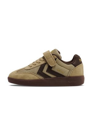 Beige lage sneaker met bruine zool, zwarte chevronstrepen, veters aan de voorkant en een klittenbandsluiting bovenop.