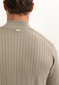 Suéter de punto acanalado en color beige con un alto cuello, etiqueta de logo discreta en la parte posterior y un ajuste ceñido con detalles texturizados.