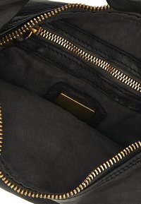 Interno di una borsa in pelle nera, con una cerniera dorata, foderatura in tessuto nero e una piccola etichetta color crema. La cerniera è allineata lungo il bordo.
