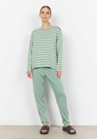 Haut rayé vert menthe à manches longues avec des détails de boutons, associé à un pantalon assorti de la même teinte, et des sandales à glissière marron foncé.