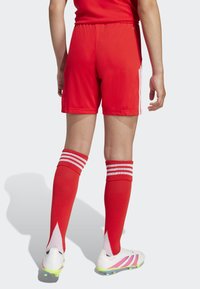 Červené futbalové šortky s elastickým pásom, v kombinácii s červenými ponožkami po kolená so bielymi pruhmi a bielymi kopačkami s ružovými akcentmi.