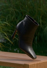 Bottine noire en simili-cuir crocodile avec un bout pointu et un talon fin, présentant une texture lisse et des éléments de design minimalistes.